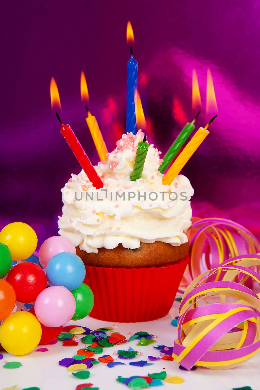 Birthday cupcake with lots of candles, party streamers and colorful confetti over purple background