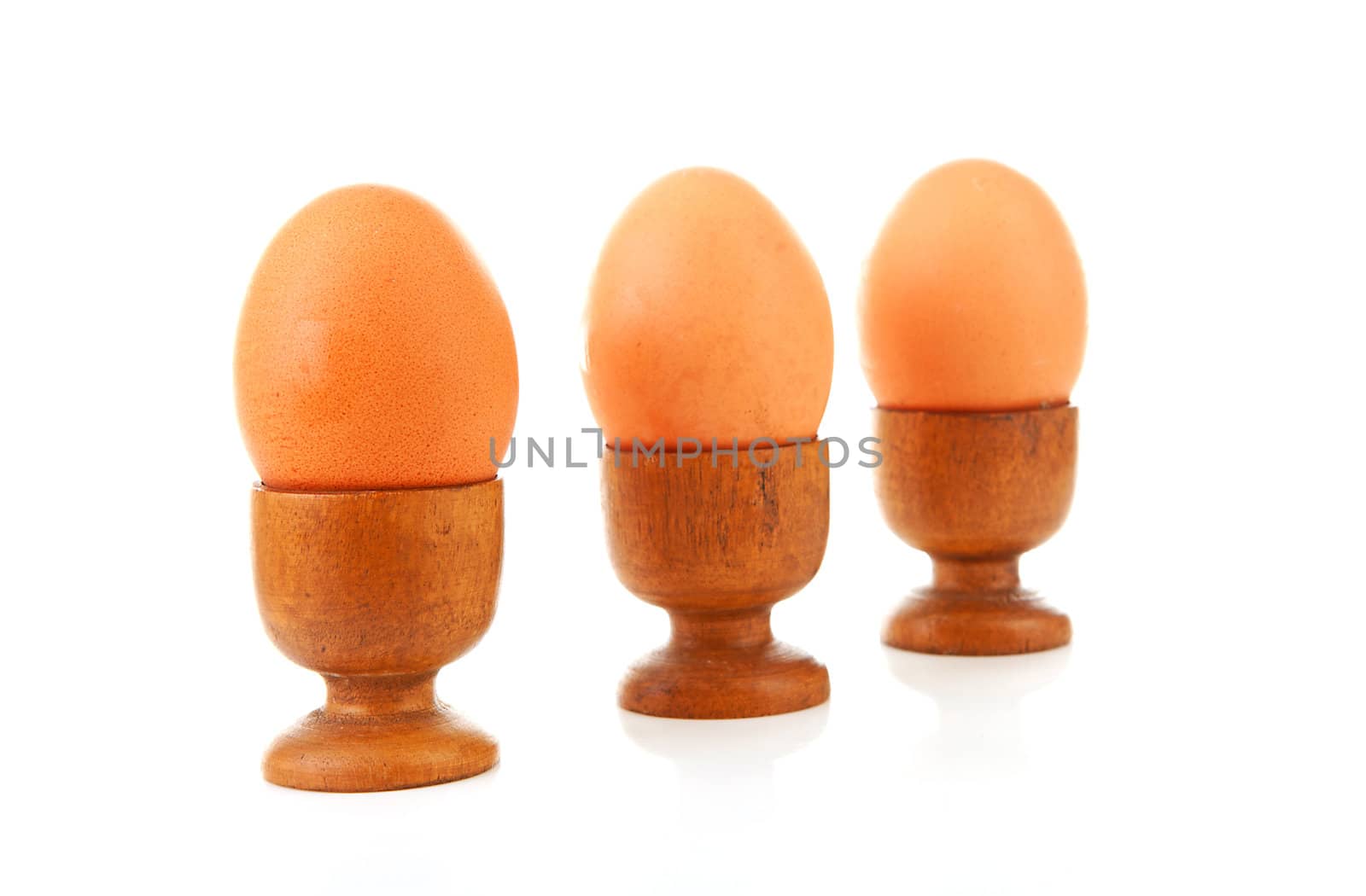 Three chicken eggs in wooden holder over white background