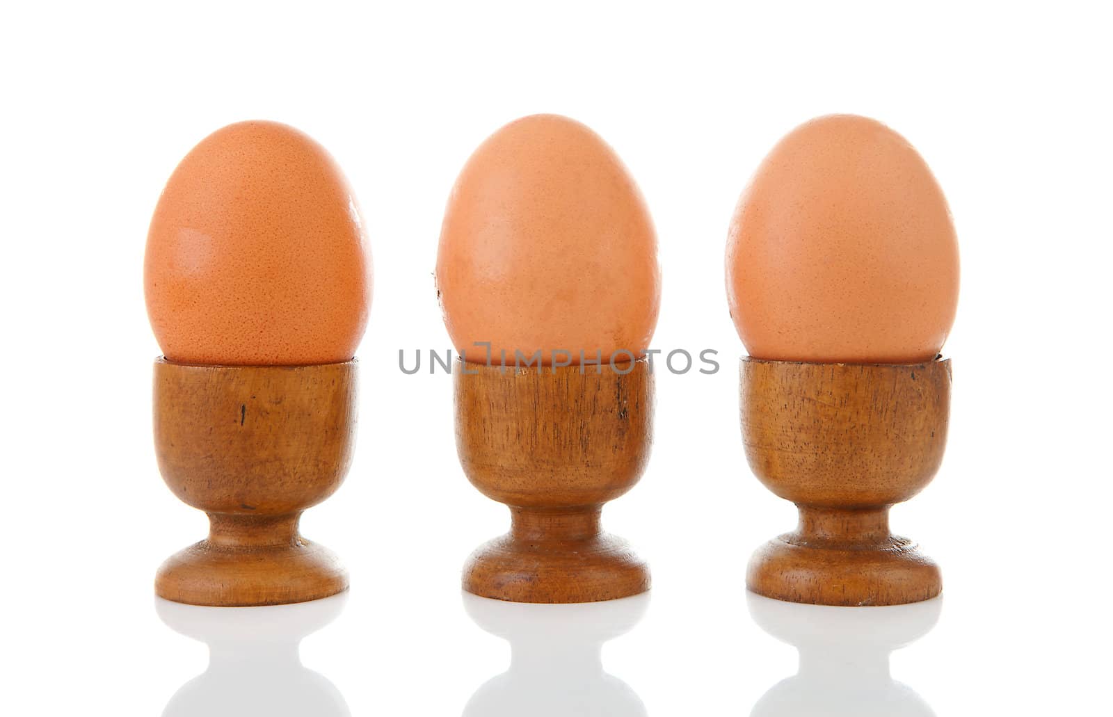 Three chicken eggs in wooden holder over white background