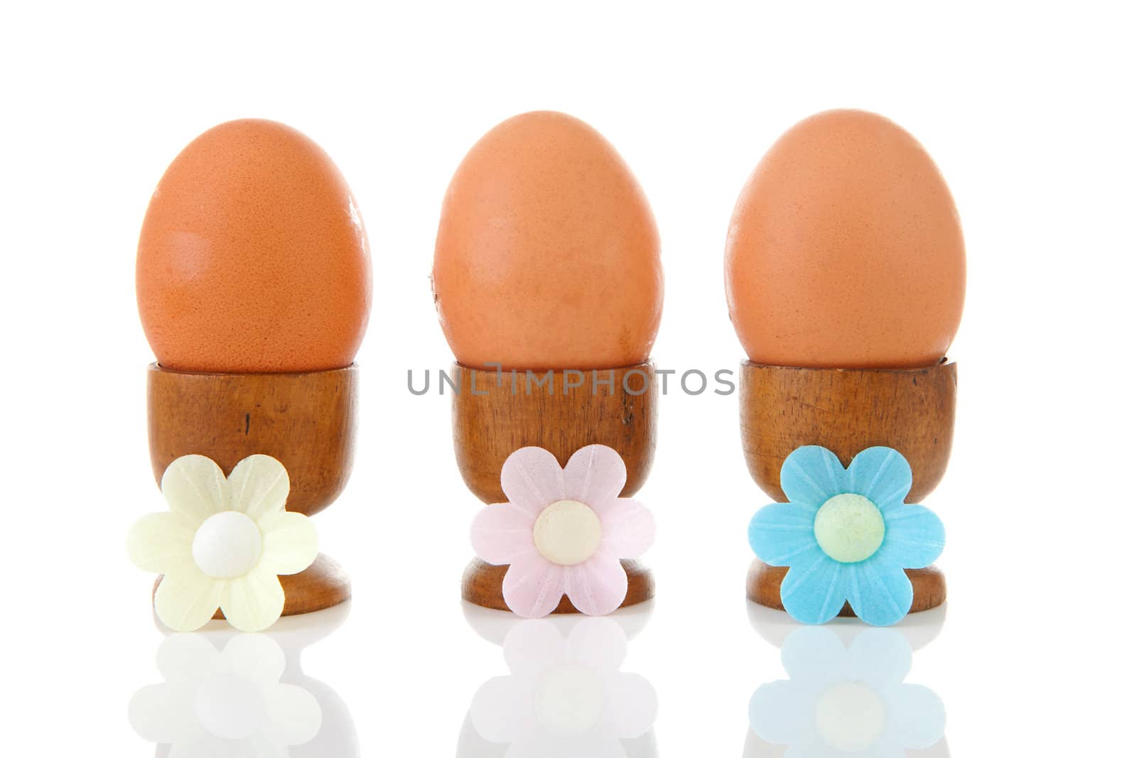 Three chicken eggs in wooden holder over white background
