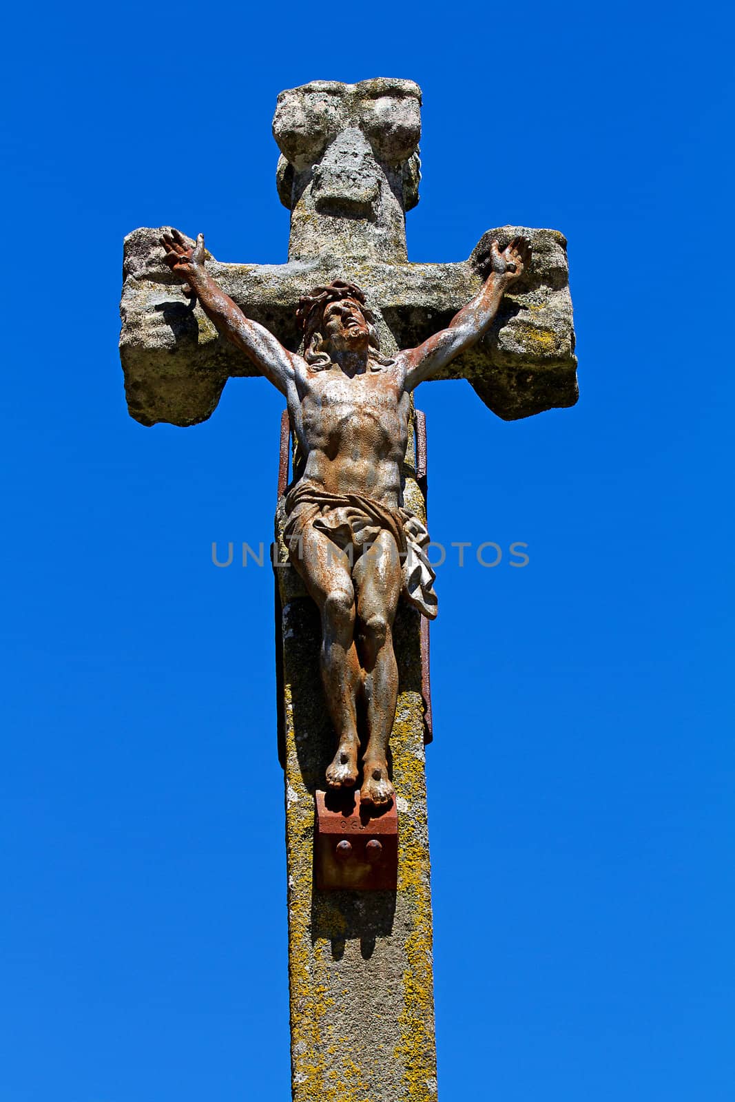 Statue of Jesus on a stone cross over blue background
