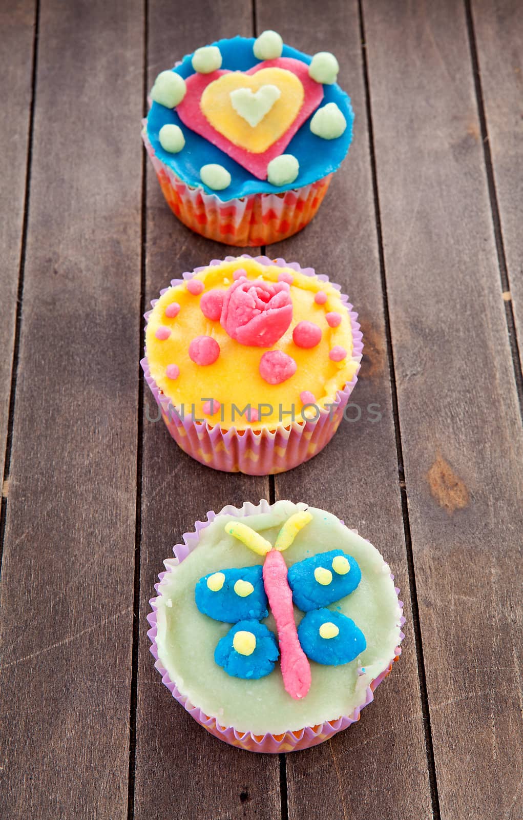 three cupcakes with marzipan decoration on wooden background