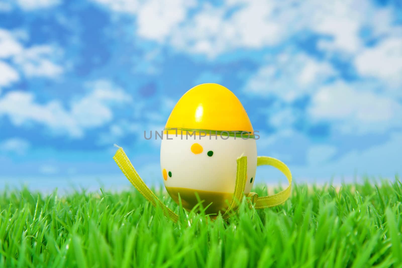 Yellow easter egg on grass against sky and clouds