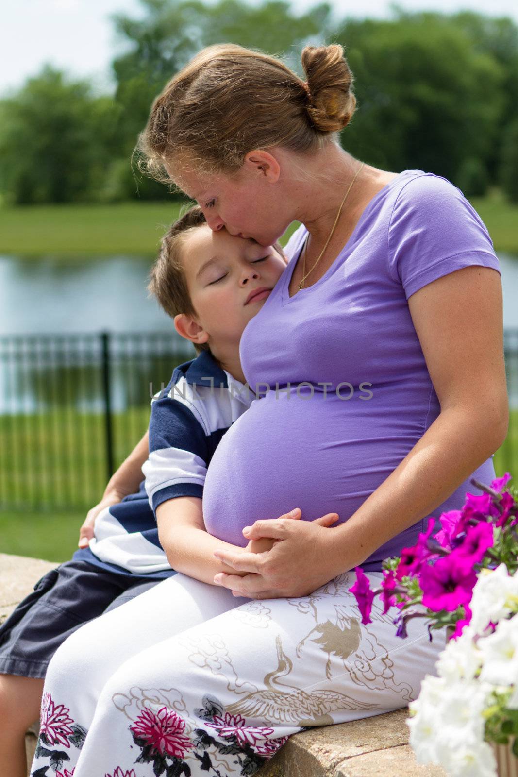 Pregnant woman holding her belly with her son while kissing him.