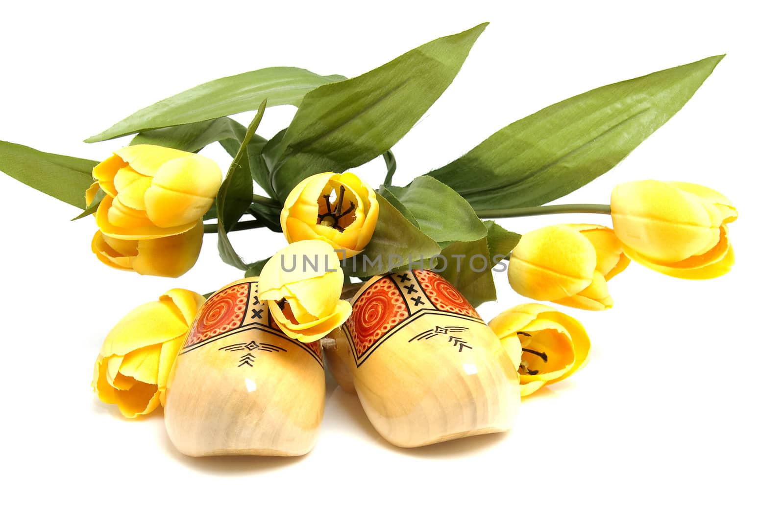 Typical Dutch wooden shoes with silk yellow tulips over white background