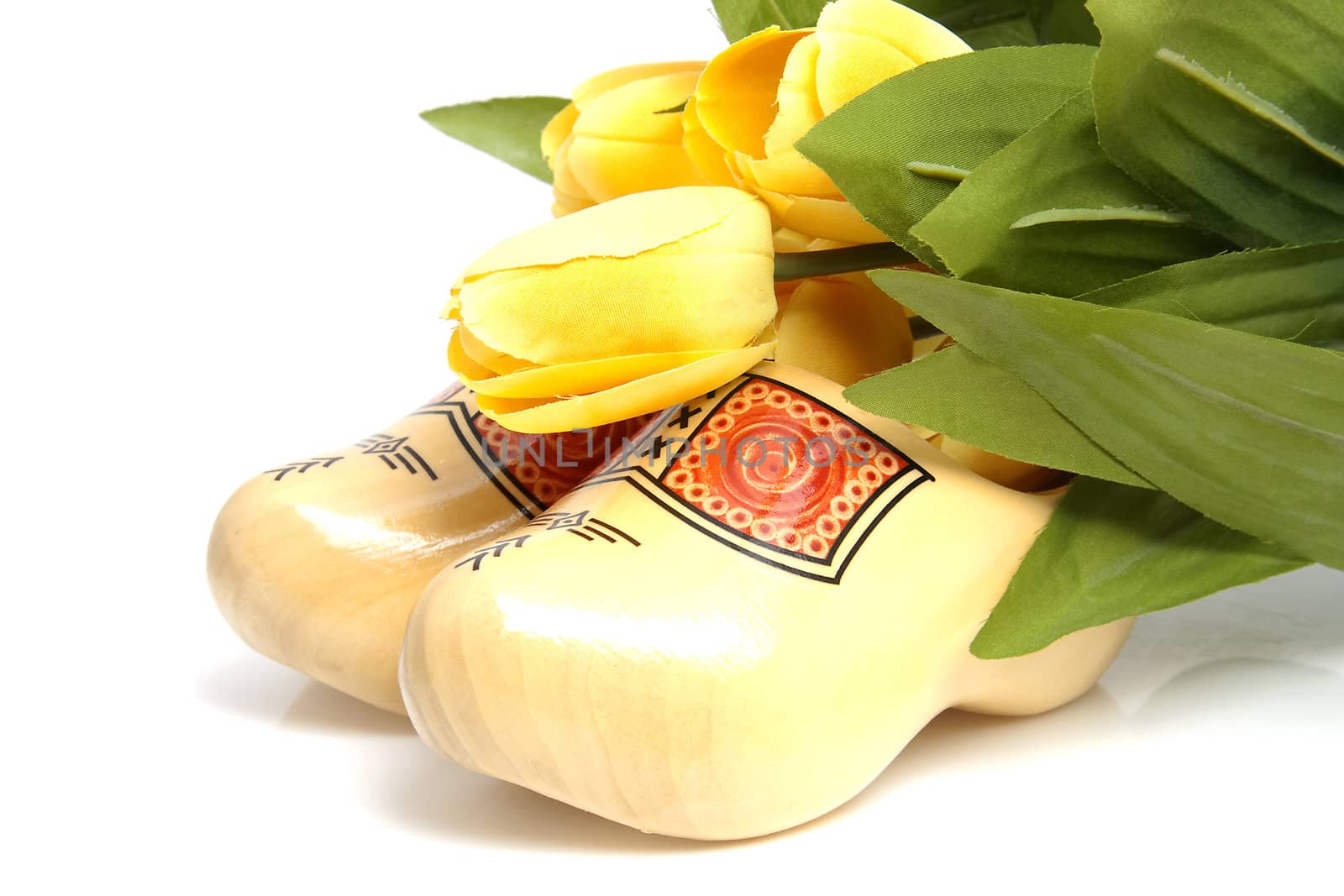 Typical Dutch wooden shoes with silk yellow tulips over white background