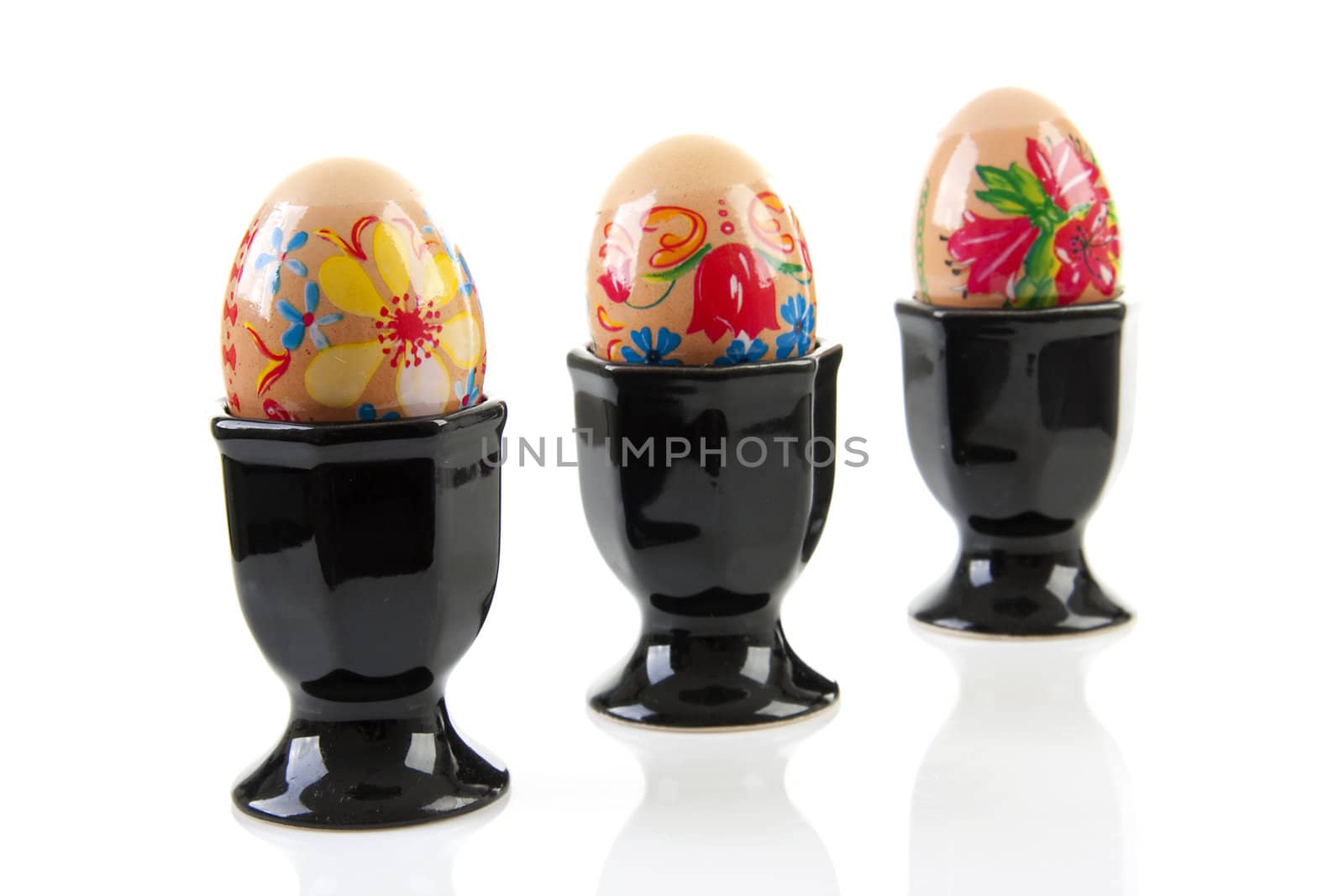 Three decorated chicken eggs in black holder over white background