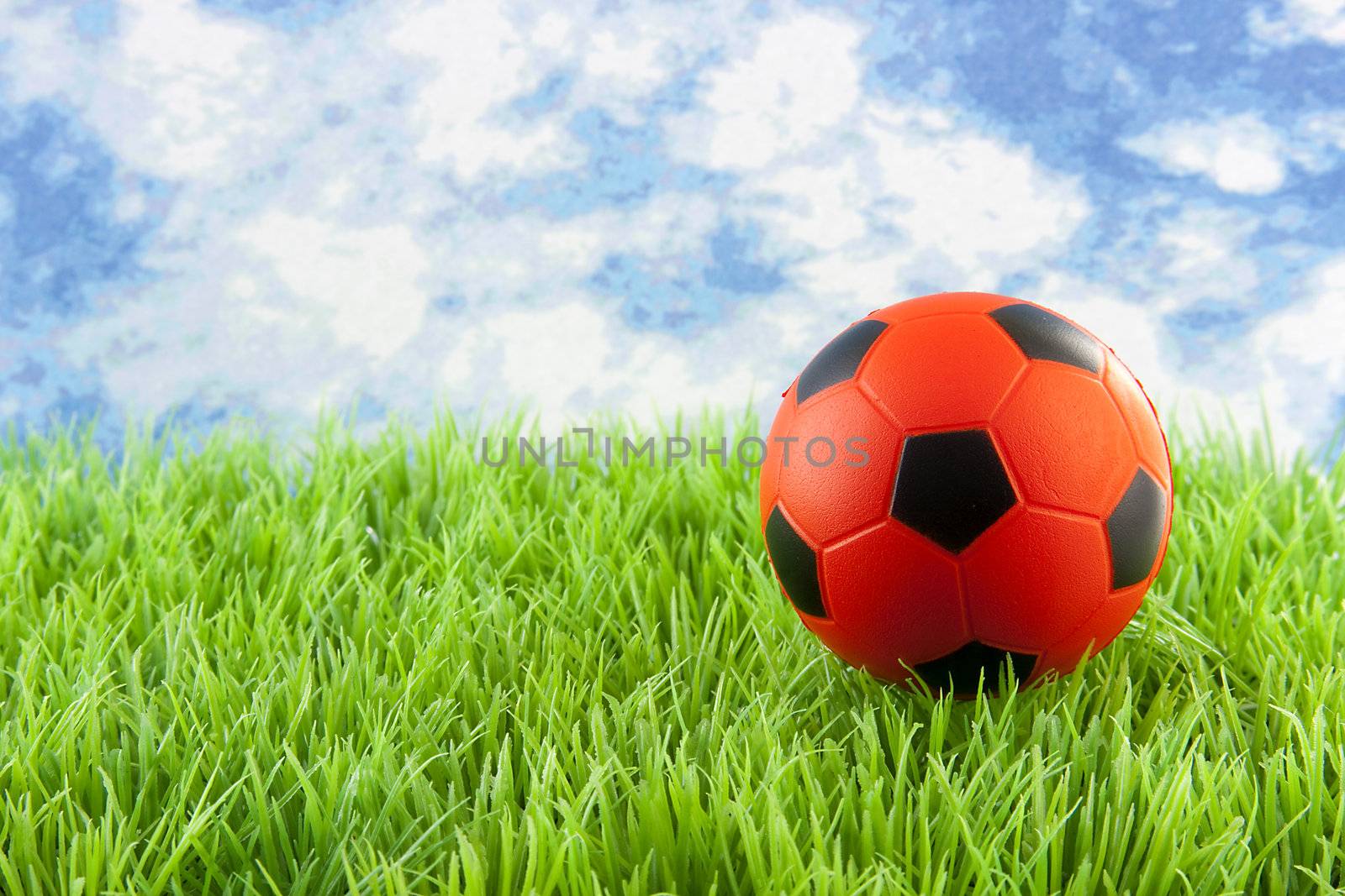 orange Soccer ball on grass against blue cloudy sky