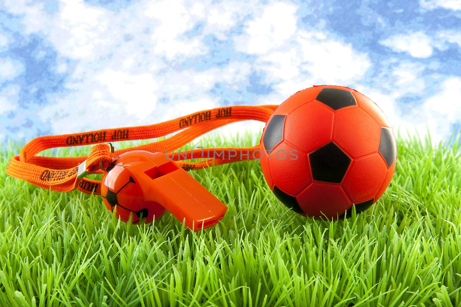 orange Soccer ball and flute on grass against blue cloudy sky