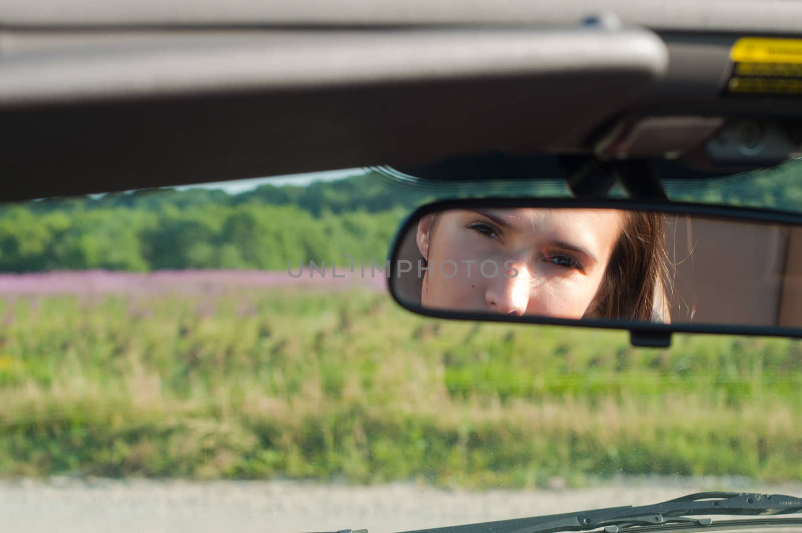 Brunette woman sitting in car and watching to rear-view mirror