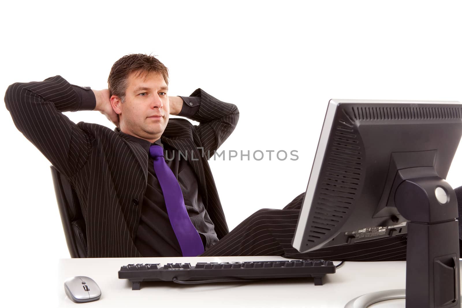 Businessman is sitting relaxed with feet on desk, looking at monitor over white background