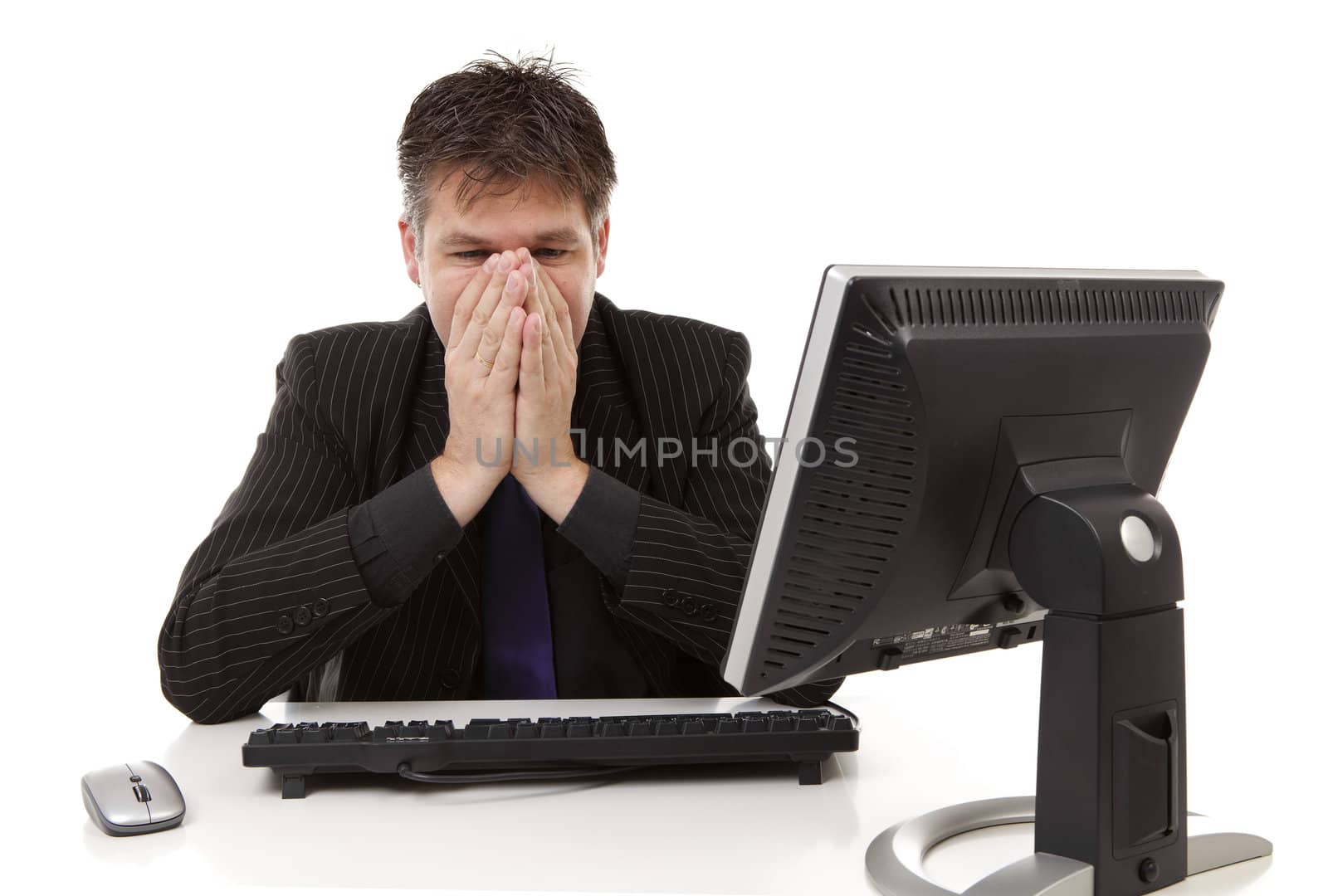 Businessman sitting behind desk is in despair, covering his mouth, over white background