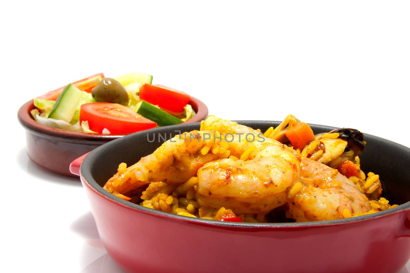 little casserole with paella and sea food over white background, behind it a bowl with salad