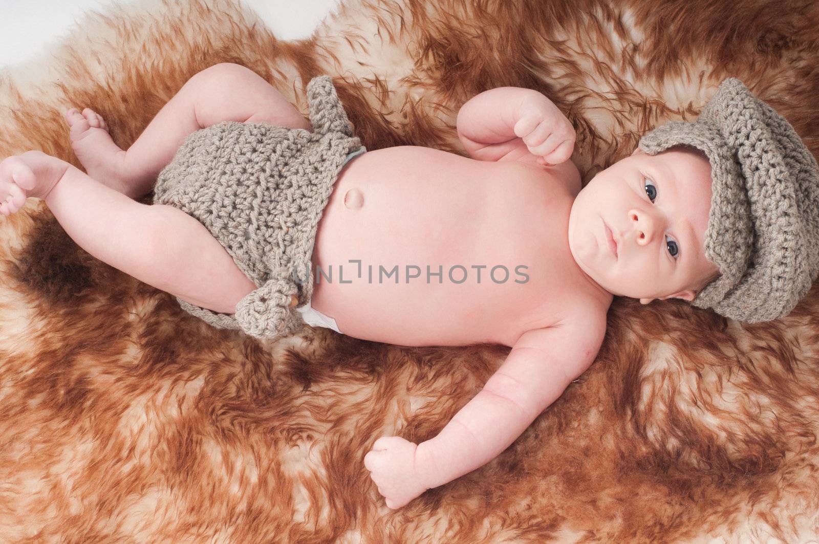 Shot of newborn baby in knitted gray clothes lying on fur