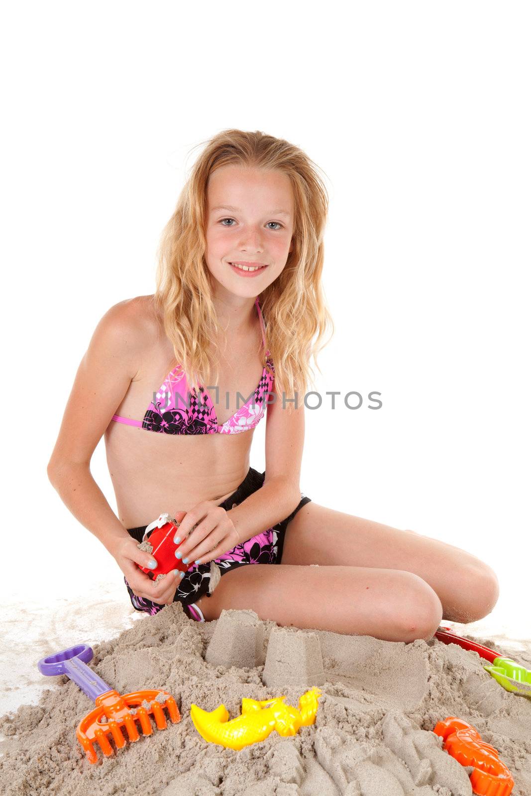 young blonde girl in beach wear playing with sand over white background