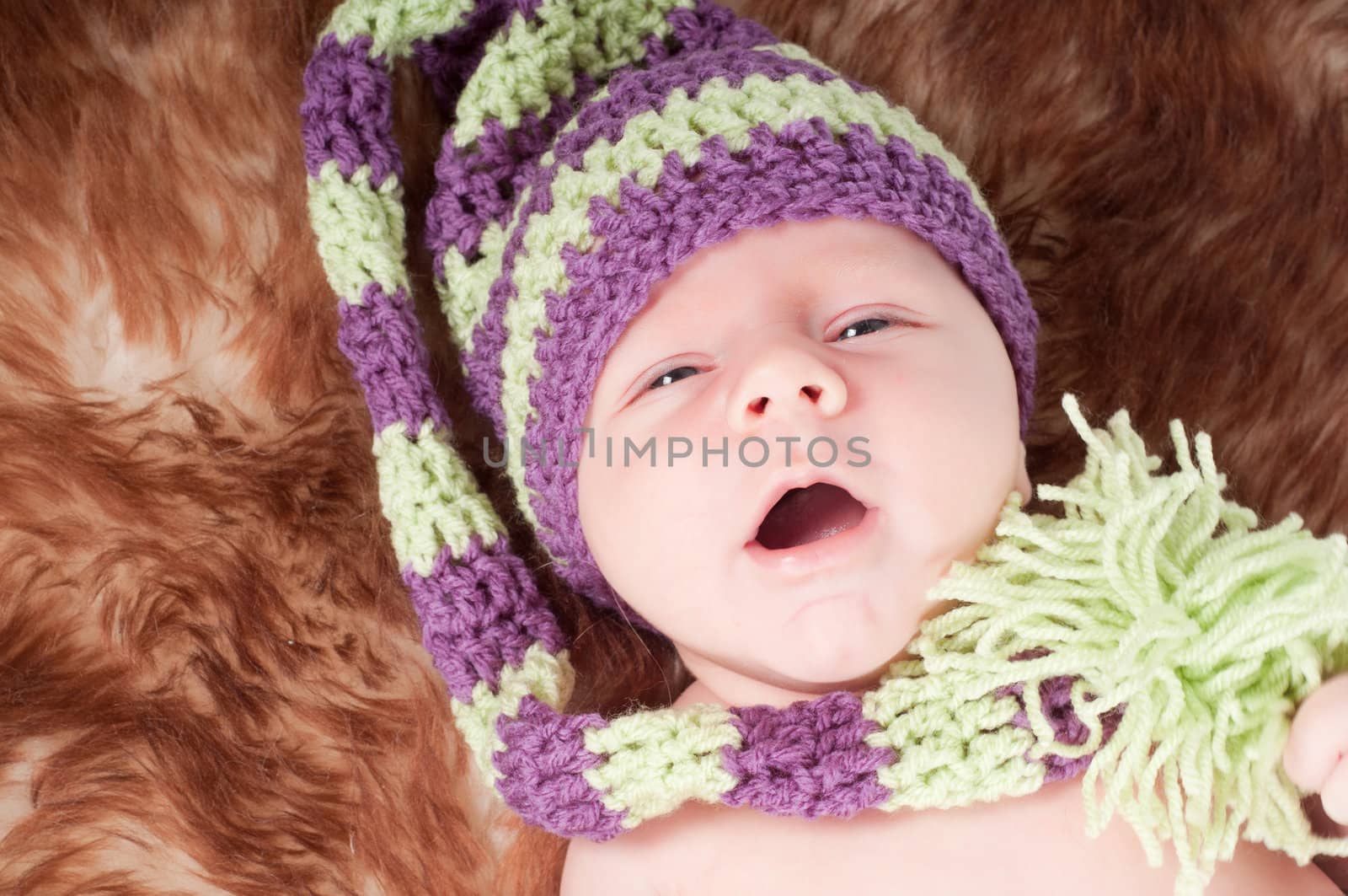 Shot of newborn baby in long knited hat lying on fur