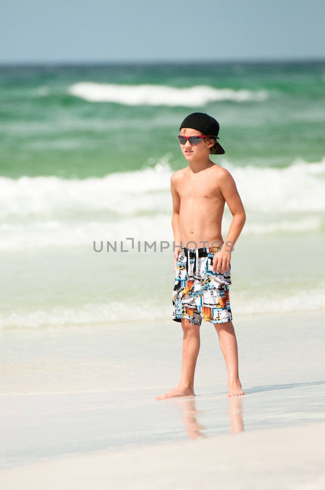 Young boy in Swim trunks at the beach with the ocean in the background.