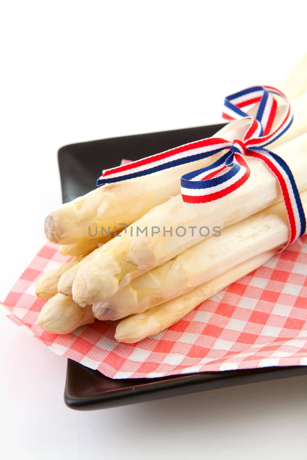 Bundle of fresh Dutch asparagus on napkin and black plate over white background