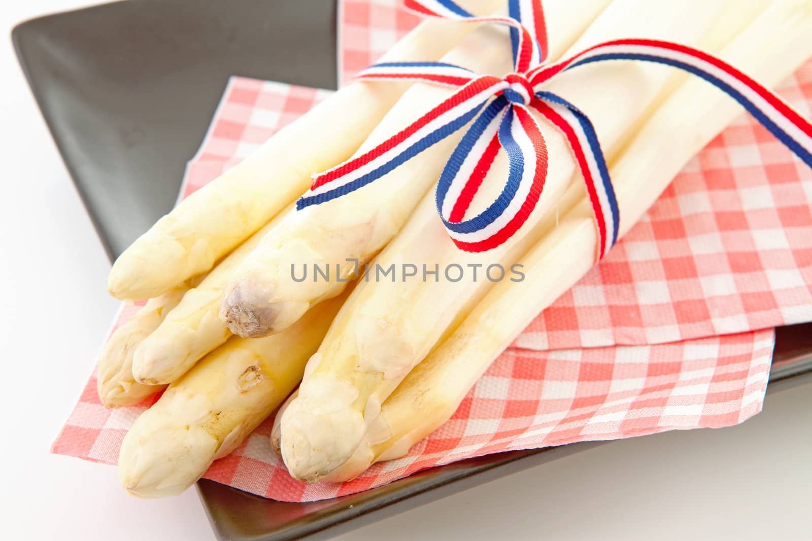 Bundle of fresh Dutch asparagus on napkin and black plate over white background
