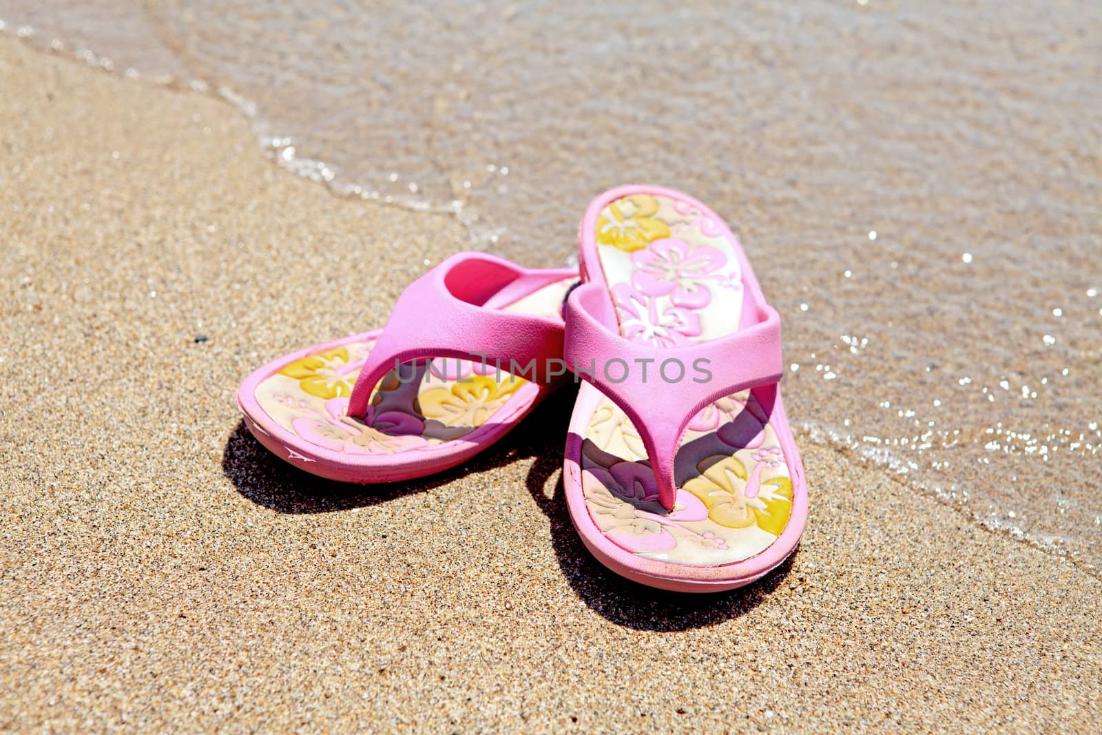 Pink summer slippers on the beach near the water