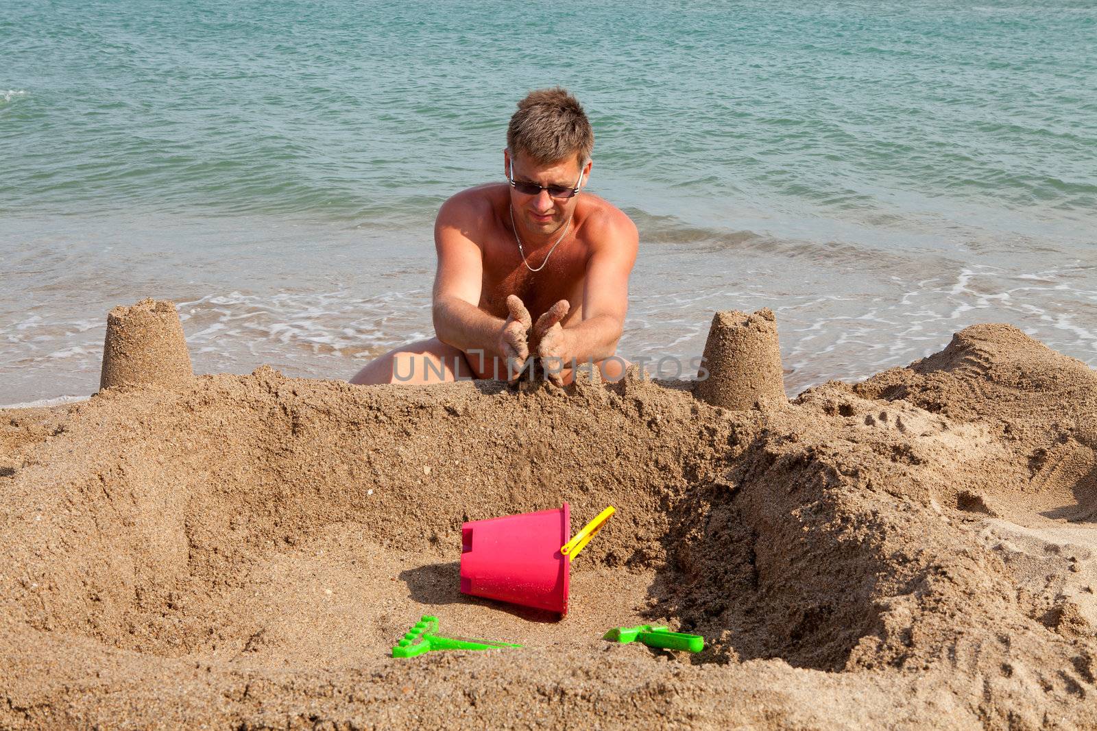 man is making sand castle on the beach near the sea