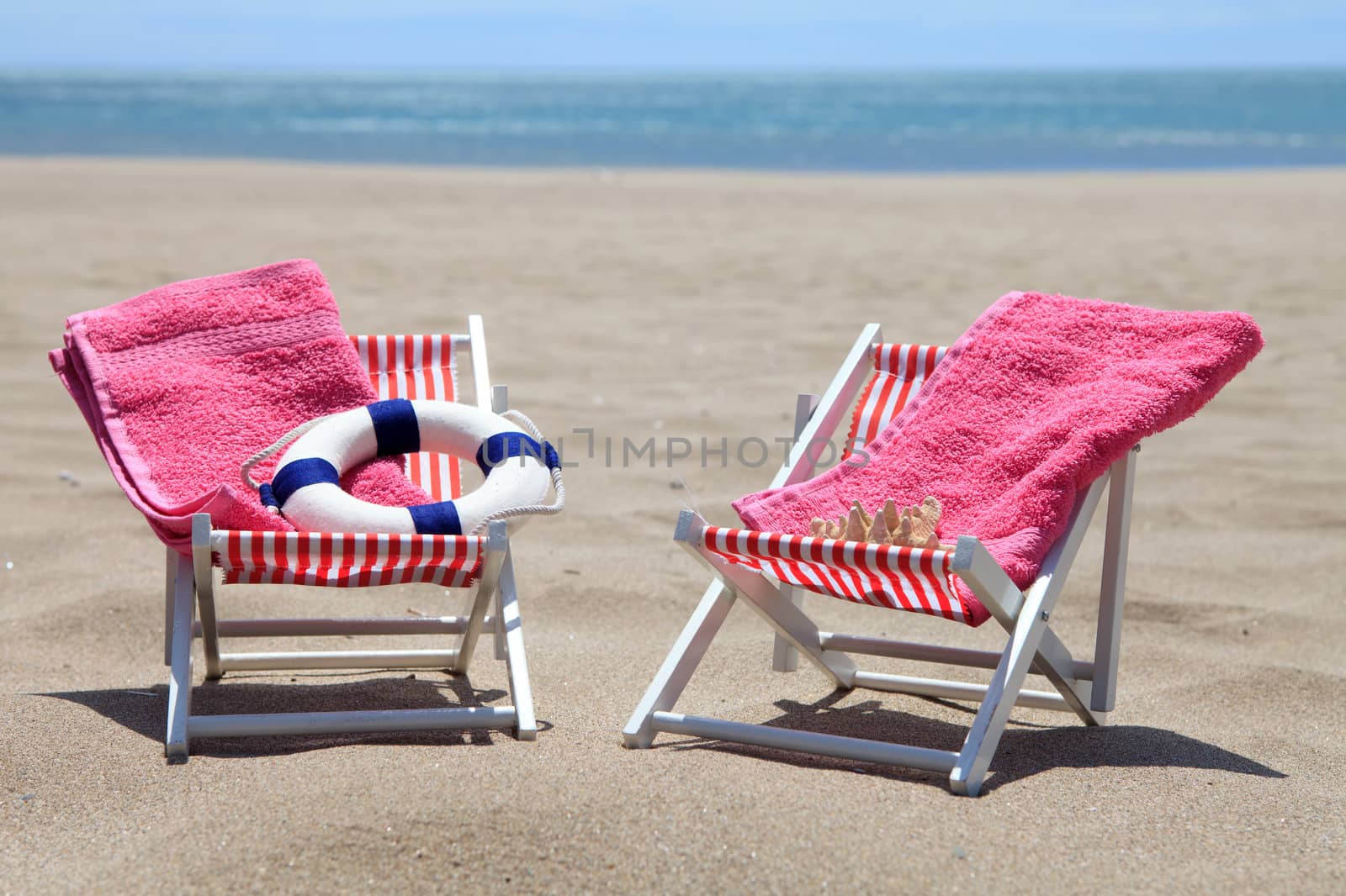 chairs on the beach with towels and life buoy