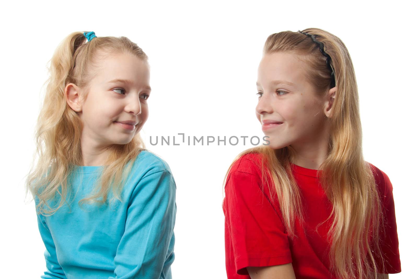 Two blonde girls sitting back to back, looking at each other, over white background