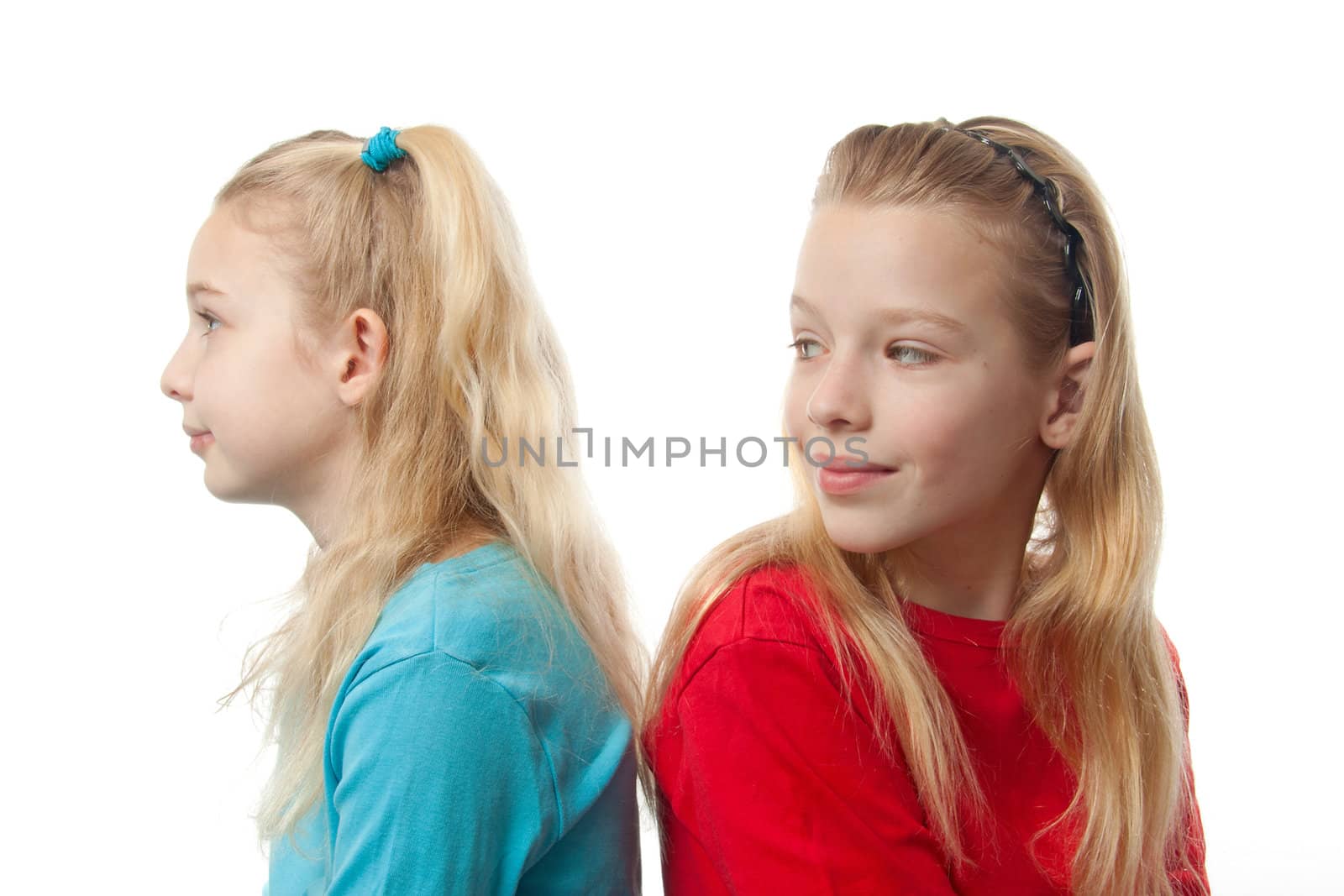 Two blonde girls sitting back to back, one is looking at the other, over white background