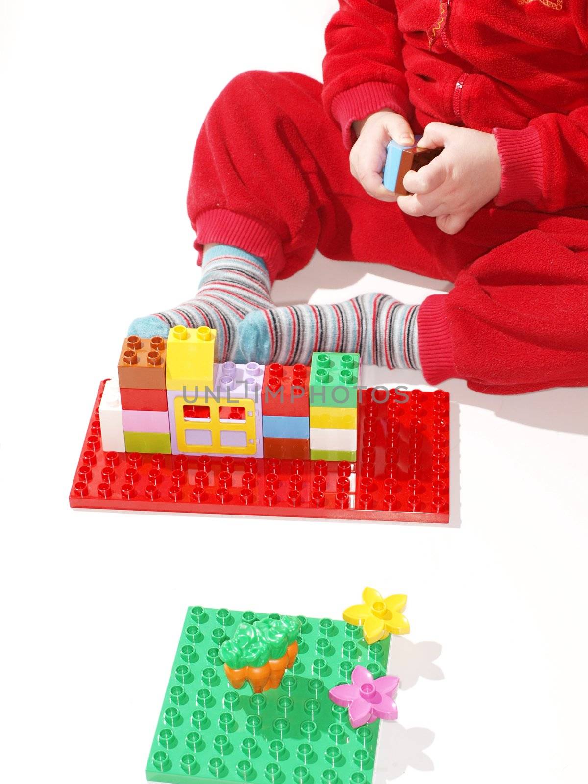 Unrecognizable kid in red, playing with colorful plastic quick build toys