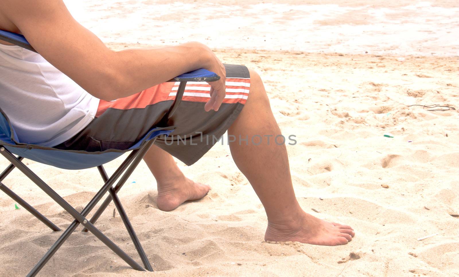 Man is sitting on a folding chair. At the beach of the sea.