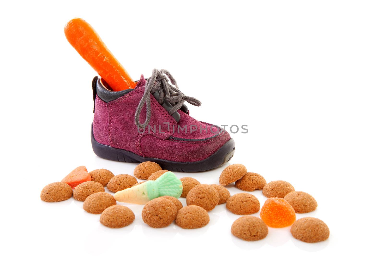 purple little children's shoe with carrot and pepernoten ( ginger nuts), traditional for Sinterklaas in the Netherlands over white backgorund