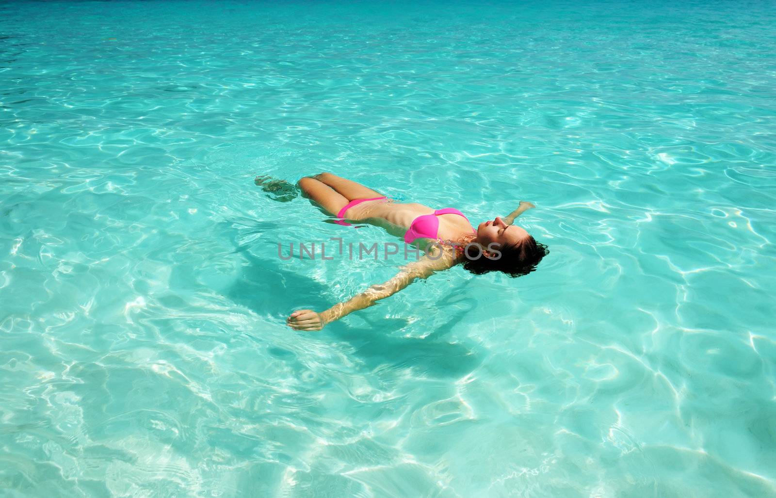 Woman in bikini lying on water at tropical beach