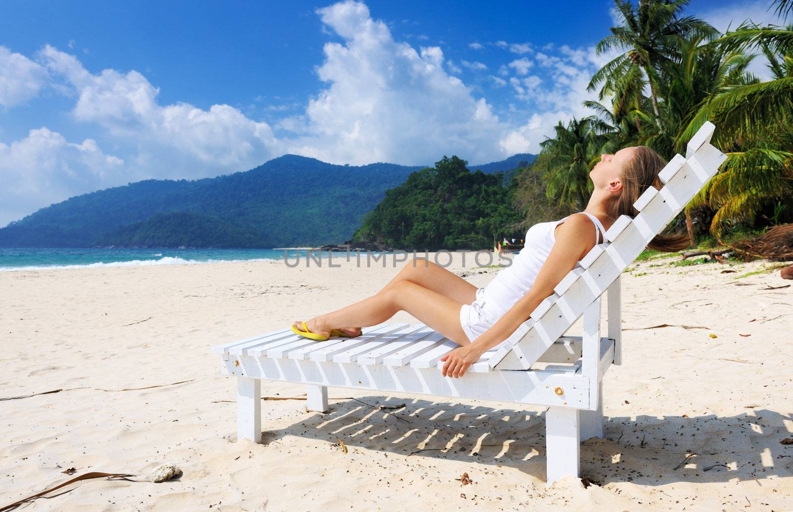 Girl on a tropical beach sitting at chaise lounge