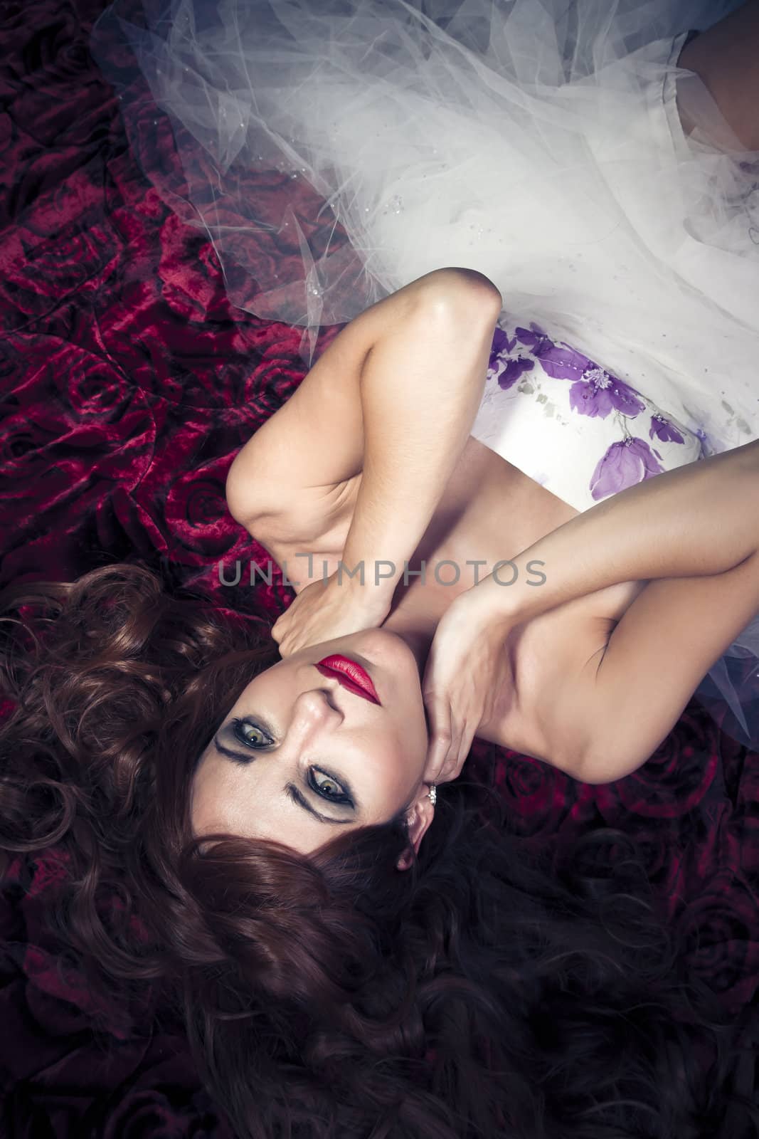 Beautiful girl lying on red roses blanket, sensual look