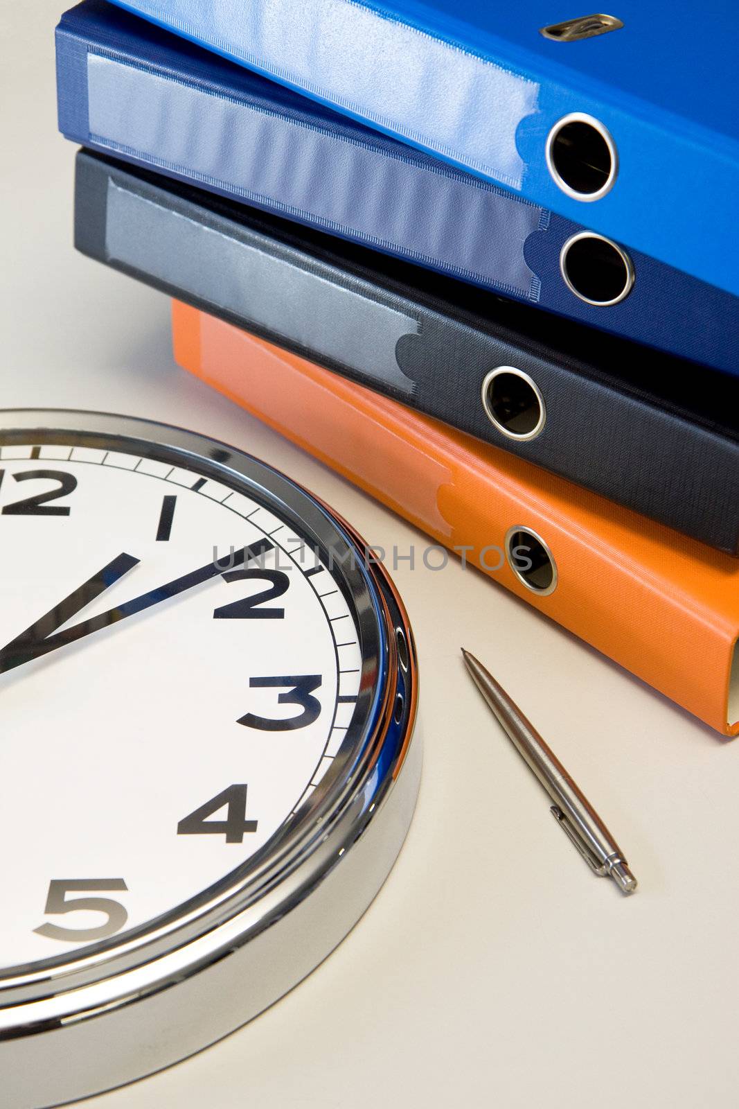 The clock and a pen in a table near colored binders in office, workplace