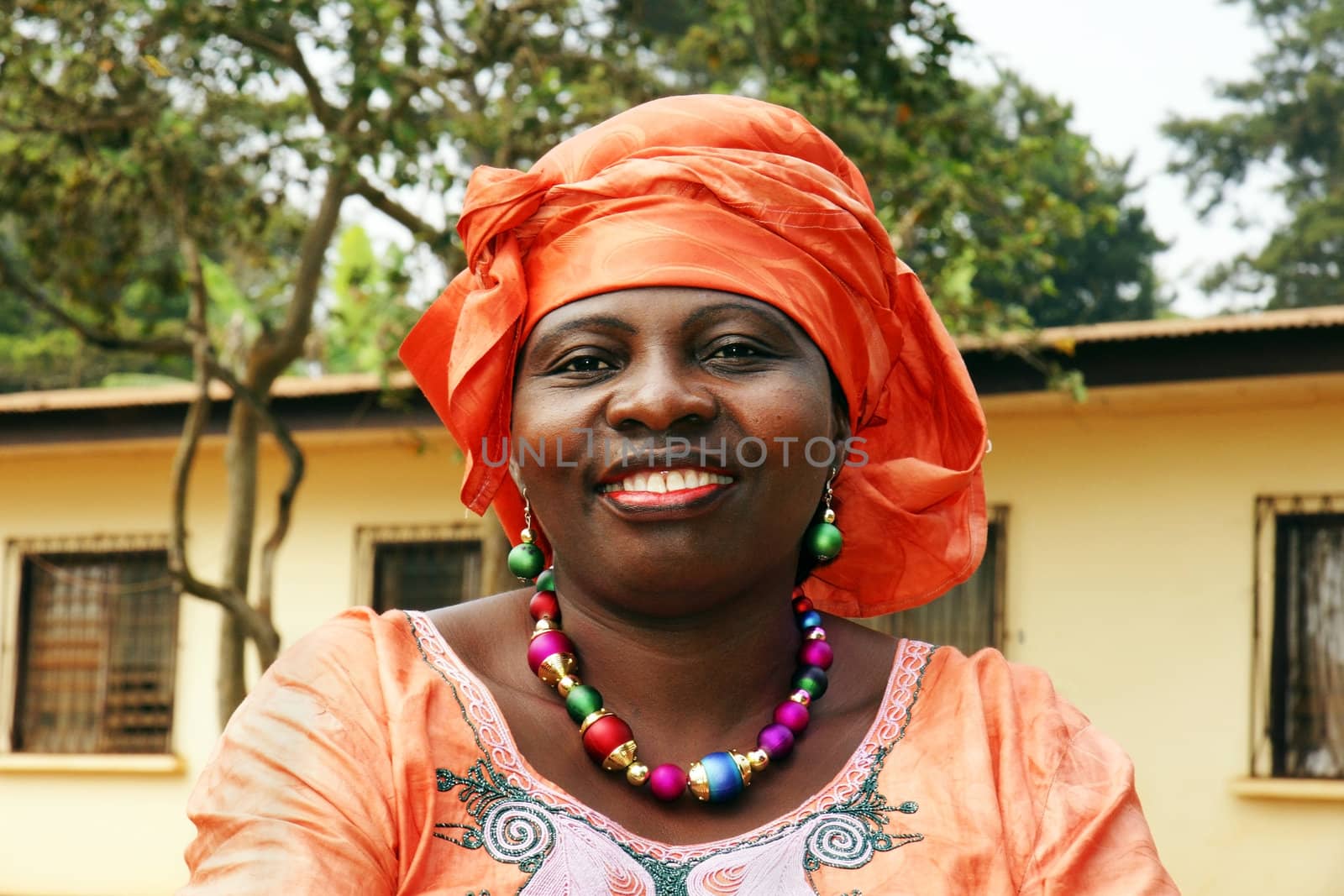 Portrait of a beautiful middle-aged black African woman smiling, wearing orange traditional clothing with scarf.