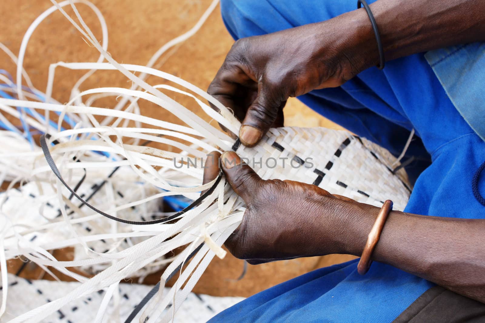 Hands of a black african worker, recovering plastic by weaving long strands to make decorative and strong belts to be reused as different objects.