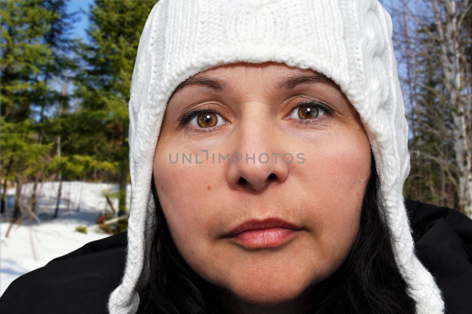 Portrait of middle aged caucasian woman enjoying winter time outdoors in nature, keeping warm with her white wool hat and black coat.
