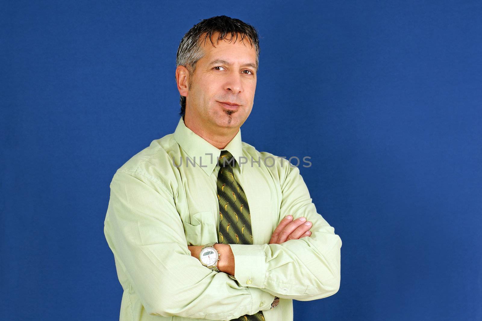 Middle age caucasian business man, can be boss, manager or other employee, arms crossed with little smile on his lips, studio shot over blue background.