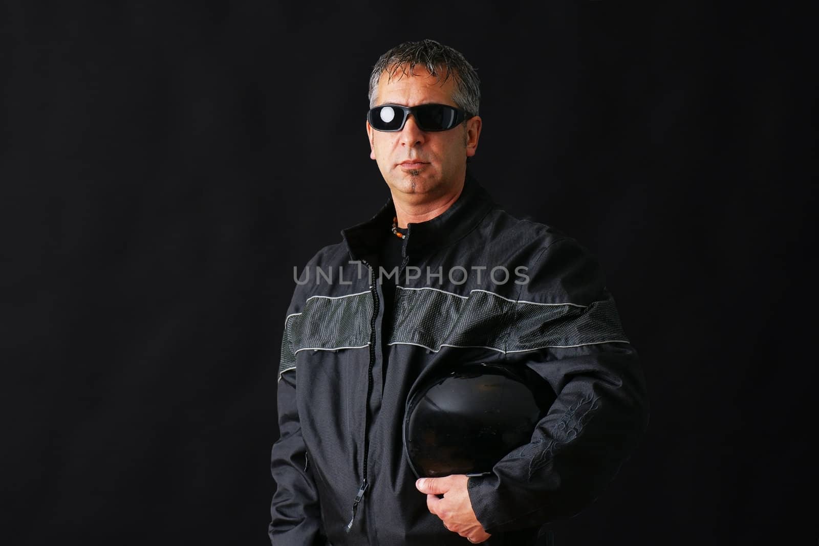 Tough looking guy with biker jacket and helmet, could be criminal, middle aged, studio shot over black.
