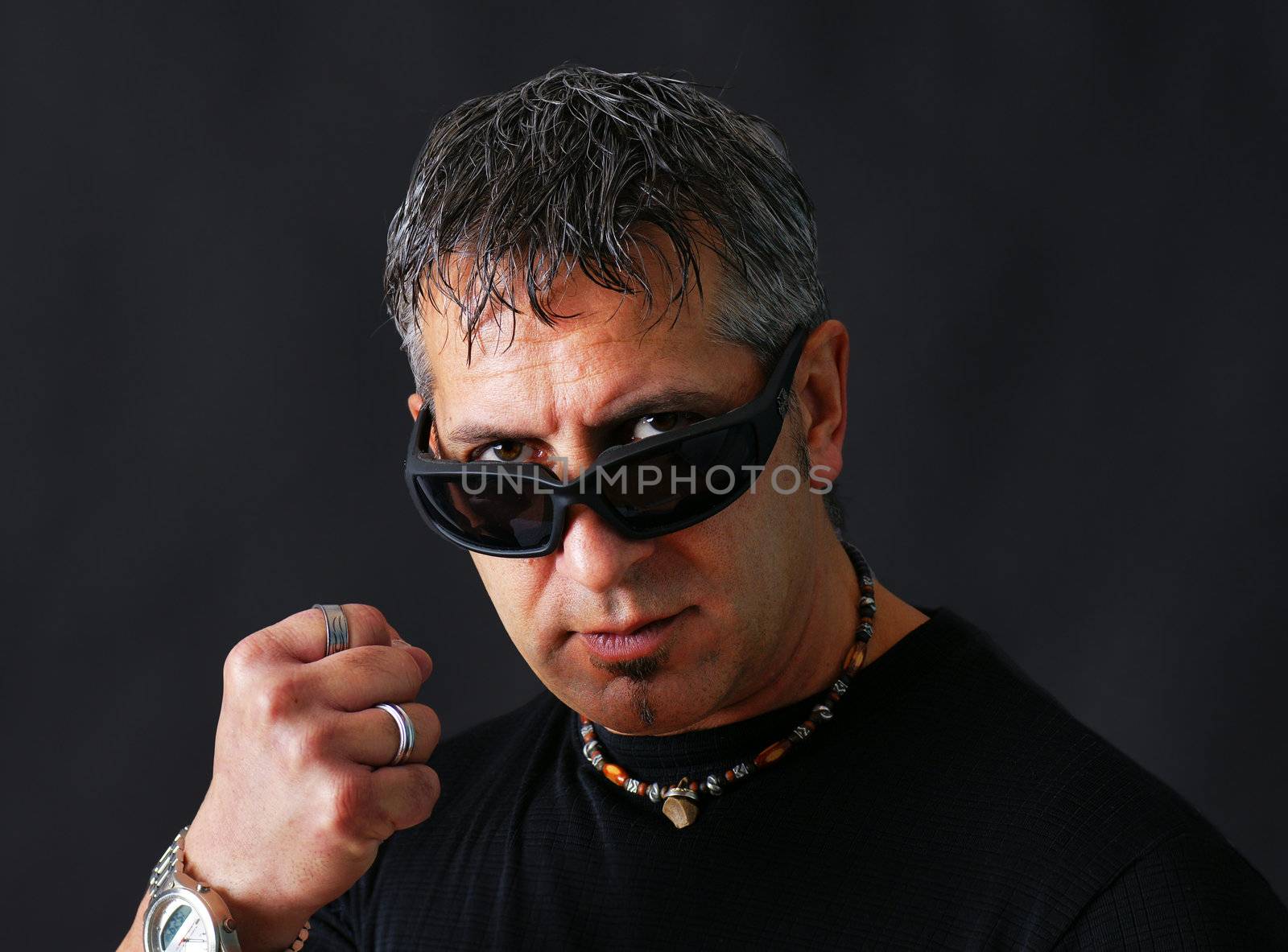 Angry tough guy or criminal with dark biker sun glasses staring at viewer and threatenig him with his closed fist.