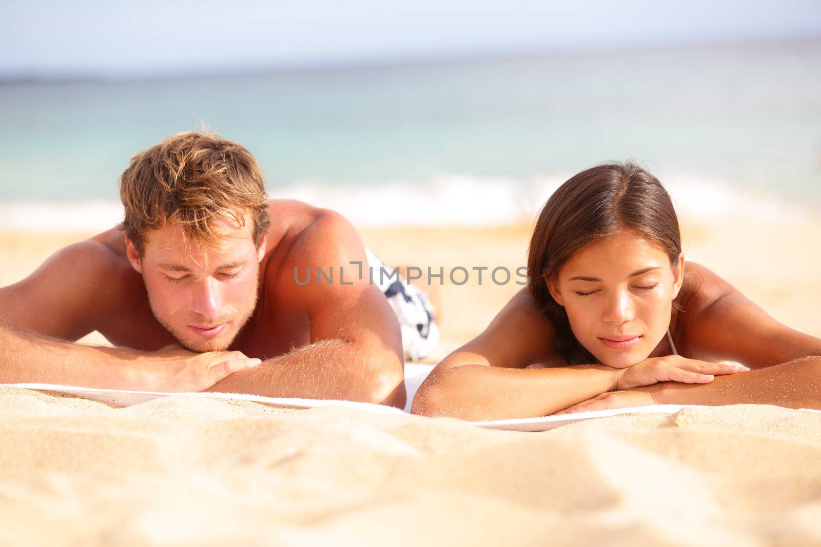 Young couple relaxing sleeping on beach sunbathing and tanning during summer vacation holidays travel. Young interracial multiethnic couple, Asian woman, Caucasian man.