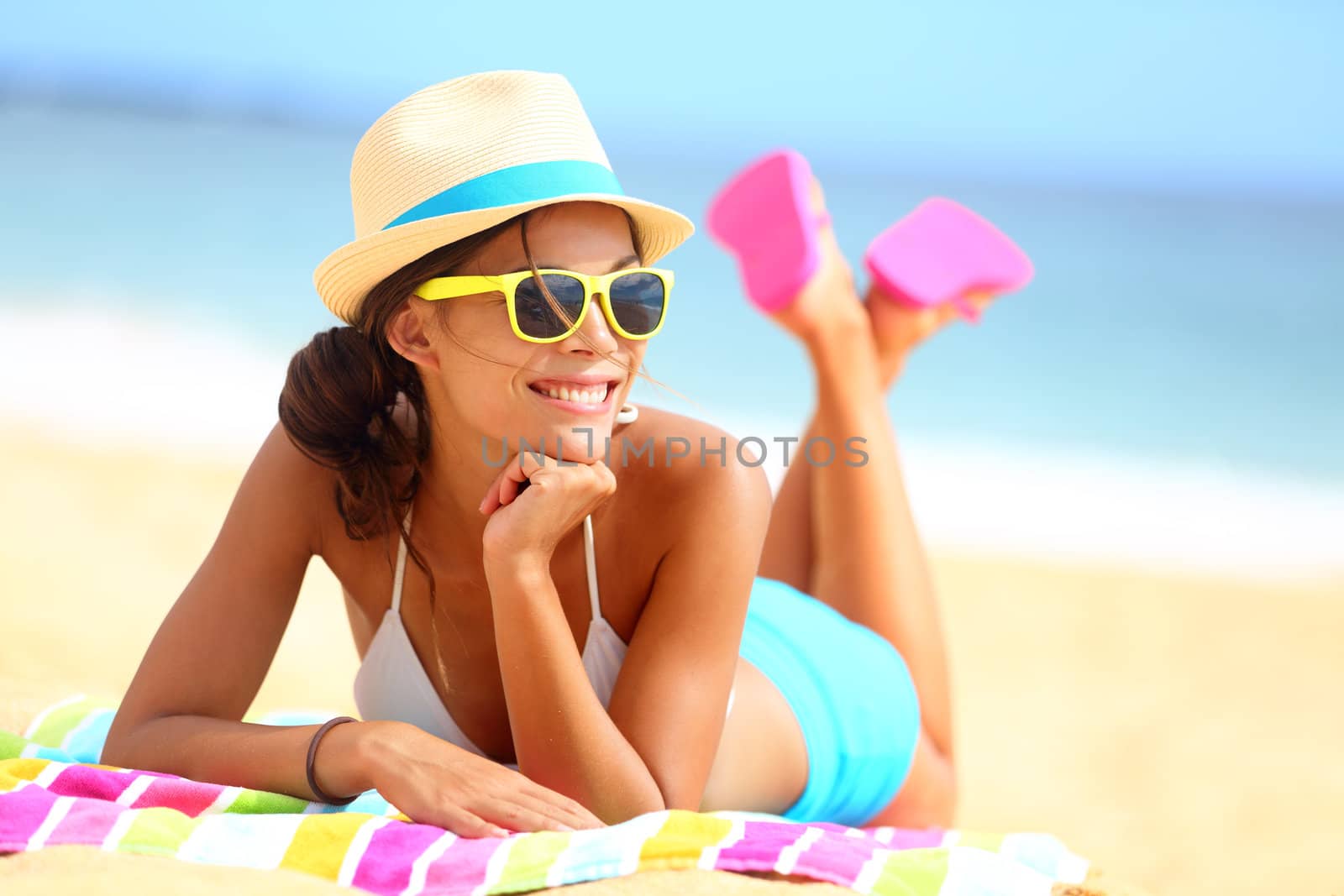 Beach woman funky happy and colorful wearing sunglasses and beach hat having summer fun during travel holidays vacation. Young multiracial trendy cool hipster woman in bikini lying in the sand.