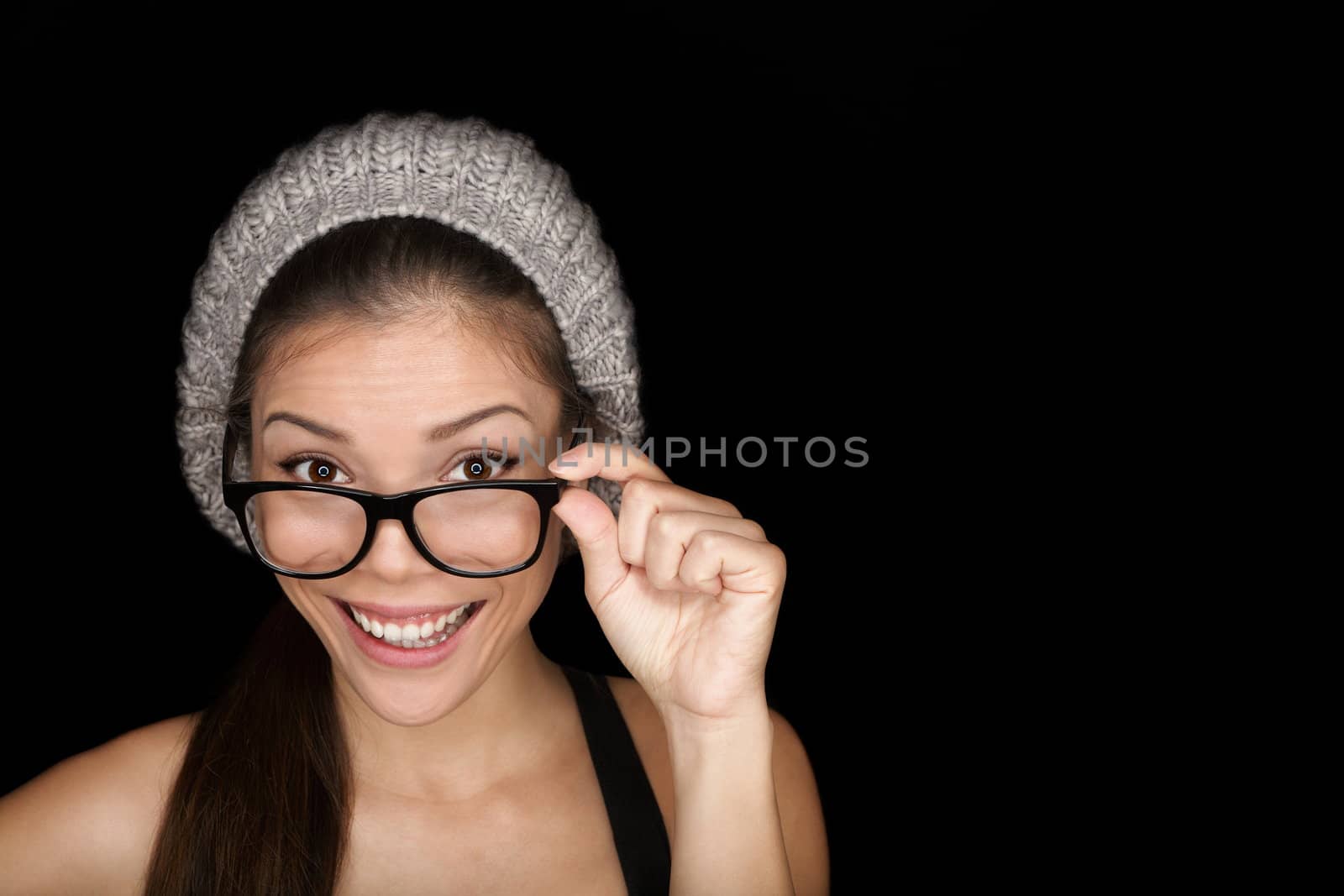Cool hipster student woman wearing eyewear glasses and knit hat isolated on black background in studio. Beautiful multiracial mixed race Asian Chinese / Caucasian female university student looking at camera smiling happy.