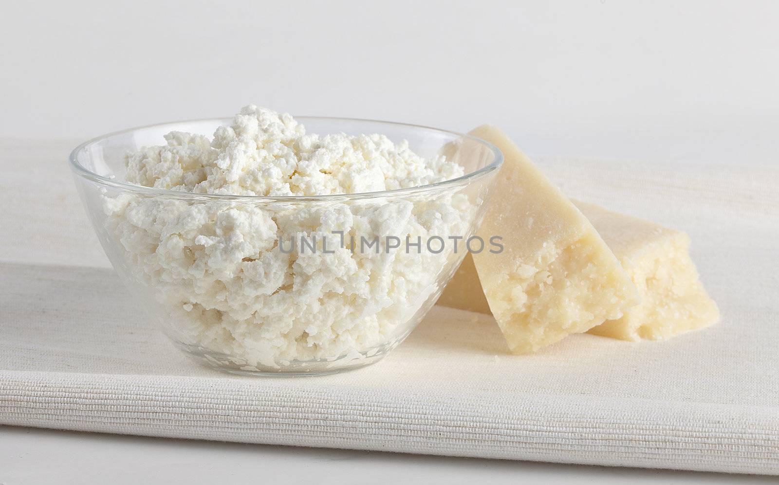 Cottage cheese in the glass bowl with hard cheese on the napkin