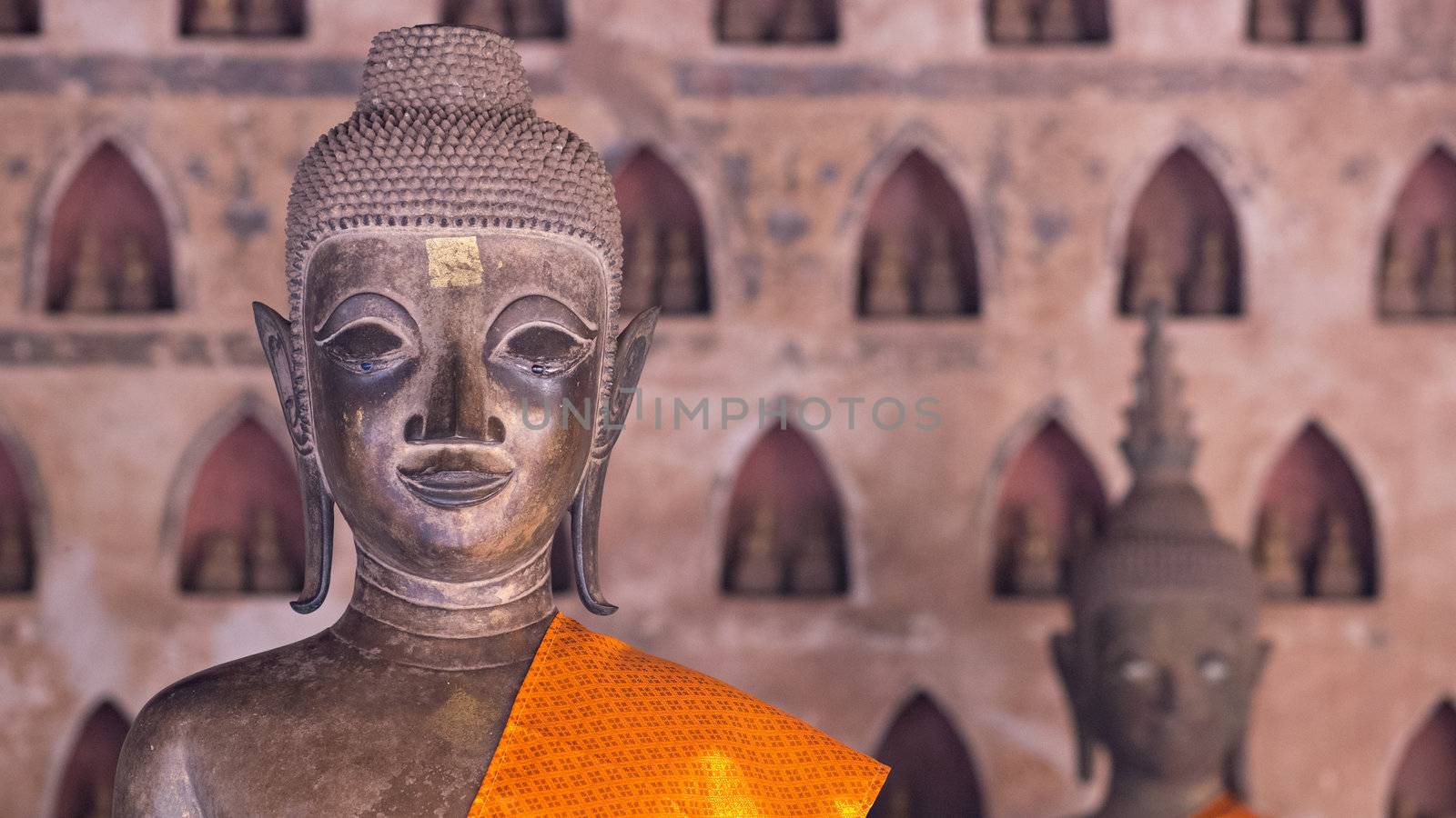 Buddha Image at Wat Si Saket in Vientiane, Laos. This temple contains 6,840 Buddha images of gold, silver and bronze, many placed in niches on the wall like in the background of this photo. Shallow depth of field with the Buddha image in the foreground in focus.