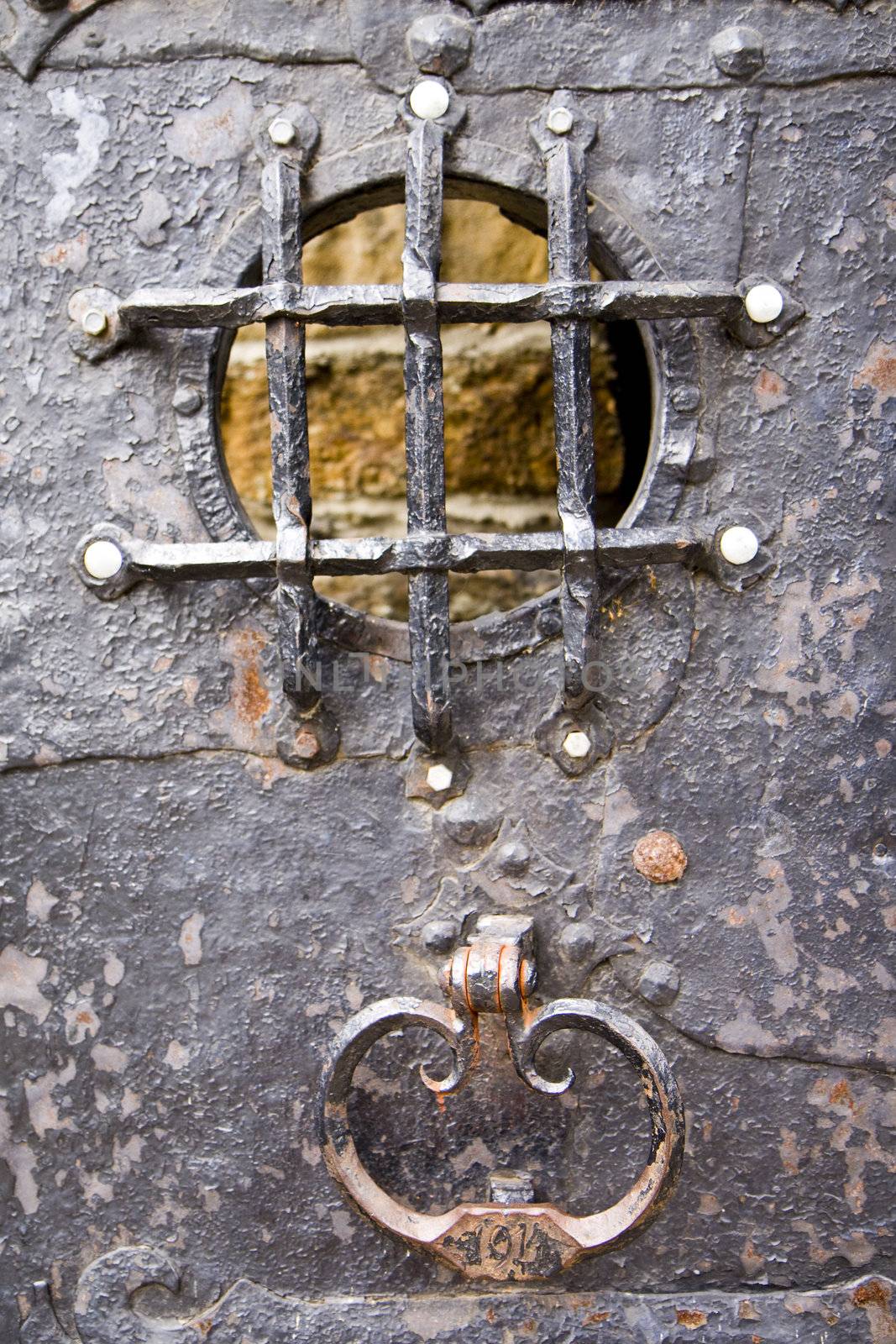 Steel medieval knocker on the old metal historic door with bars