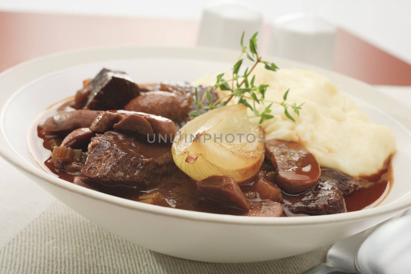 Braised beef with mushrooms and onion, cooked in red wine and served in a bowl with mashed potato.