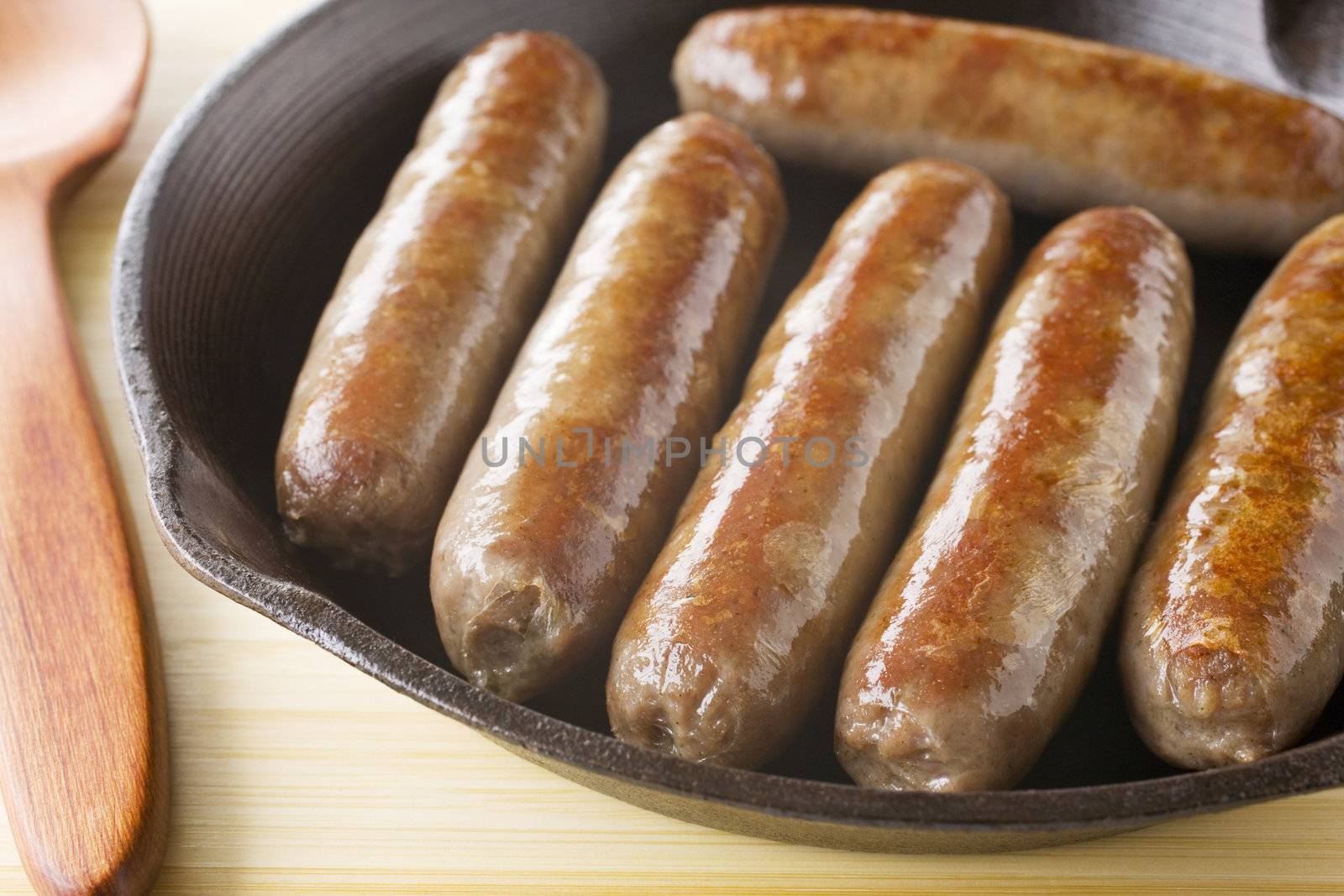 Fresh chunky sausages sizzling an a cast iron skillet.