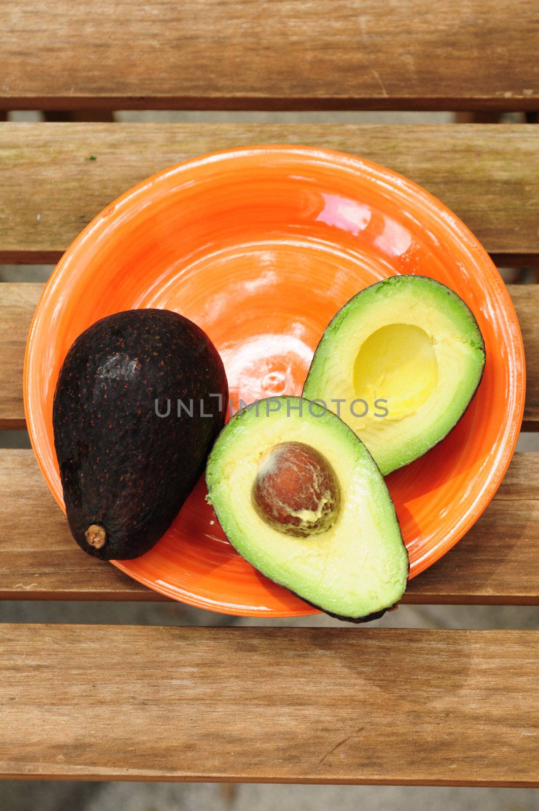 One whole and one sliced avocado on an orange plate